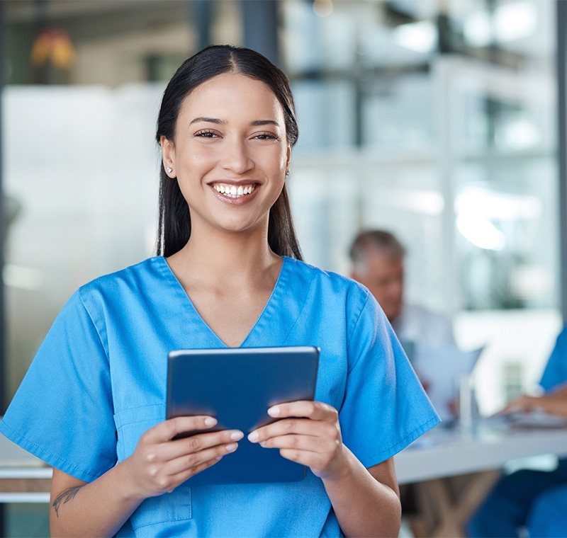 An allied healthcare professional in scrubs stands in a bright medical office, reviewing patient information on a tablet and preparing for a clinical appointment.