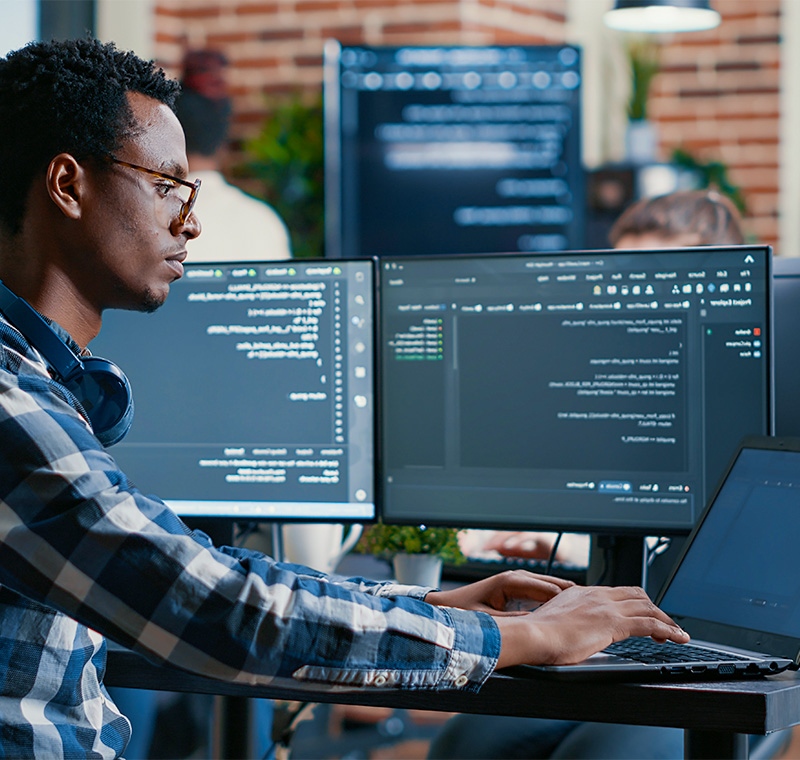 An information security systems professional works in a high-tech operations center, analyzing system data and monitoring cybersecurity dashboards on multiple screens to protect network infrastructure and sensitive information.