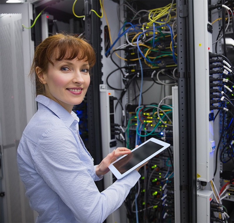 An IT security and network technician monitors multiple computer screens displaying code and network data, ensuring system security and maintaining network performance in a modern tech environment.